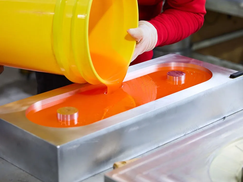 Mitarbeiter gießt oranges Polyurethan aus einem Eimer in eine Stahlform