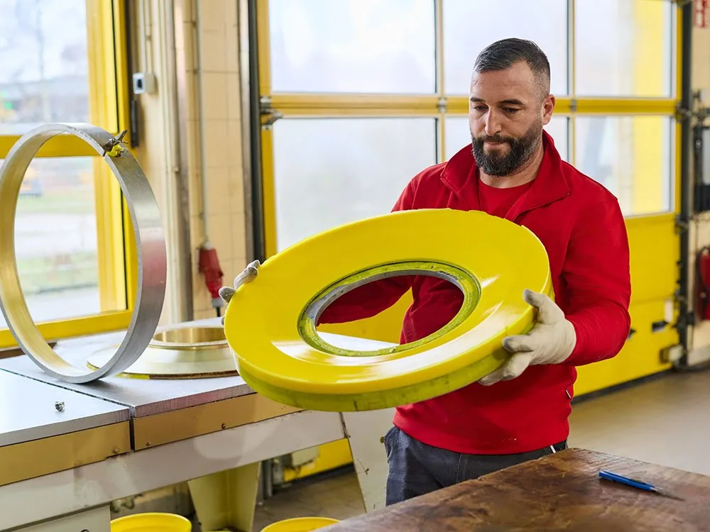Mitarbeiter hält einen gelben Gieß-Elastomer-Ring in der Fertigung